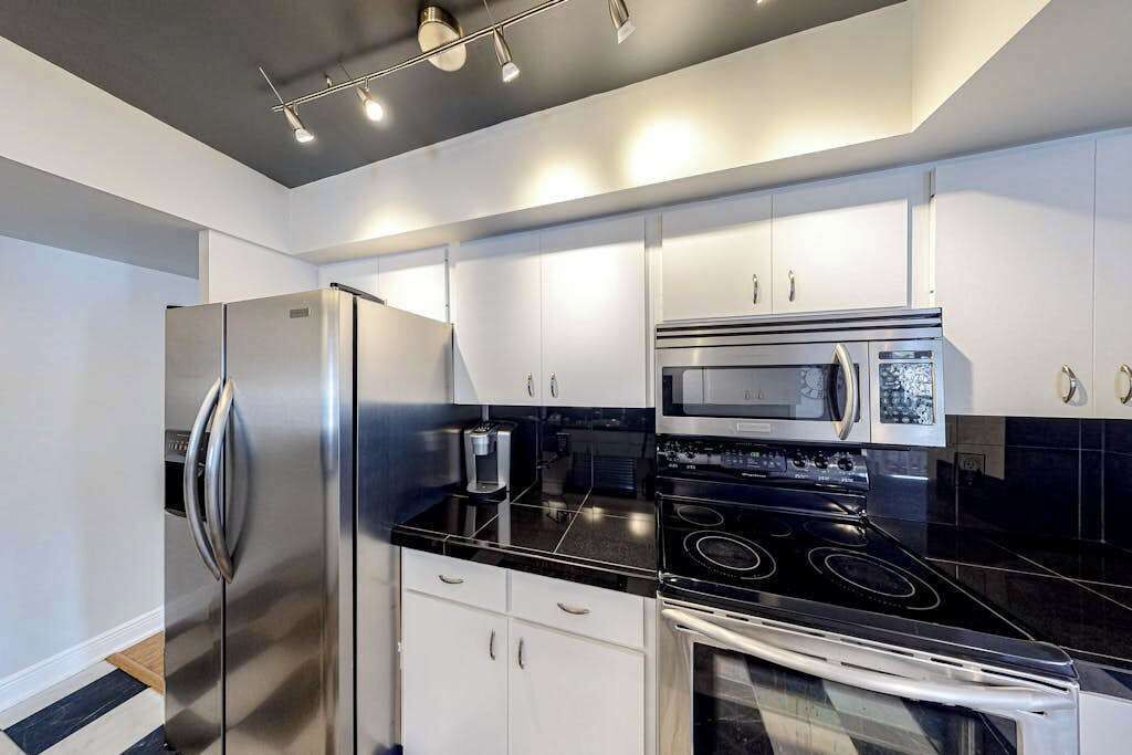 Cocina moderna con electrodomésticos de acero inoxidable, armarios blancos y encimeras negras.