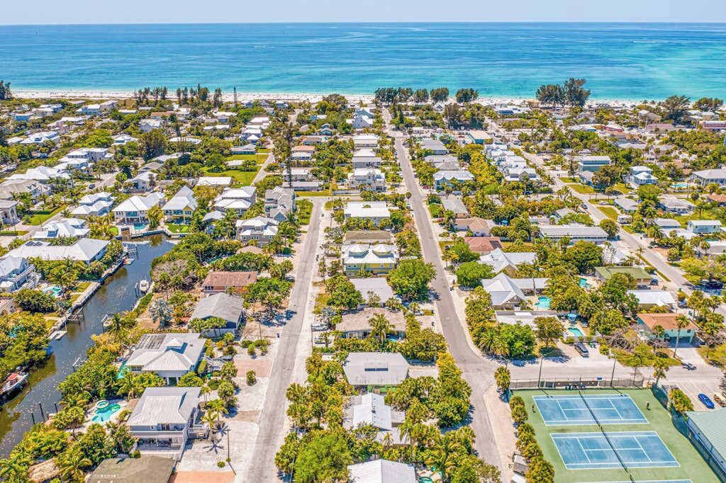 An aerial view of a coastal residential area with houses, a marina, and a tennis court.