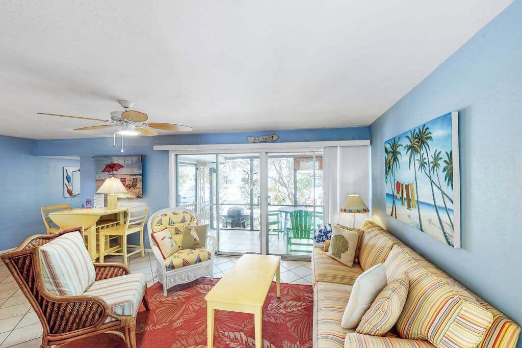 A living room with a ceiling fan, a sofa, a chair, a table, and a painting on the wall.