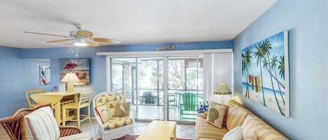 A living room with a ceiling fan, a sofa, a chair, a table, and a painting on the wall.