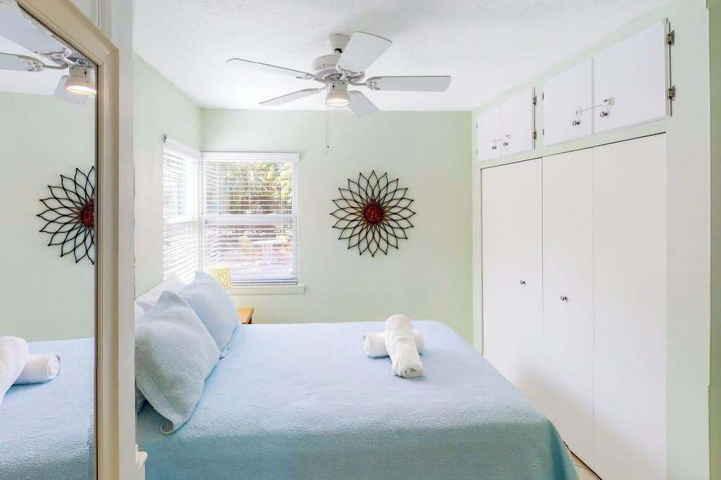 A bedroom with a bed, a ceiling fan, a window with blinds, and a wardrobe.