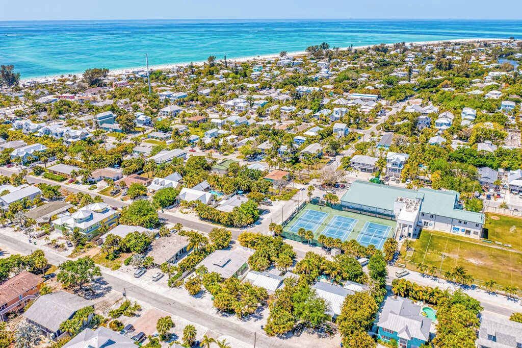 An aerial view of a coastal residential area with houses, a tennis court, and a beach.