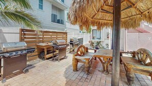 Un patio exterior con una parrilla, muebles de madera y un techo de paja.