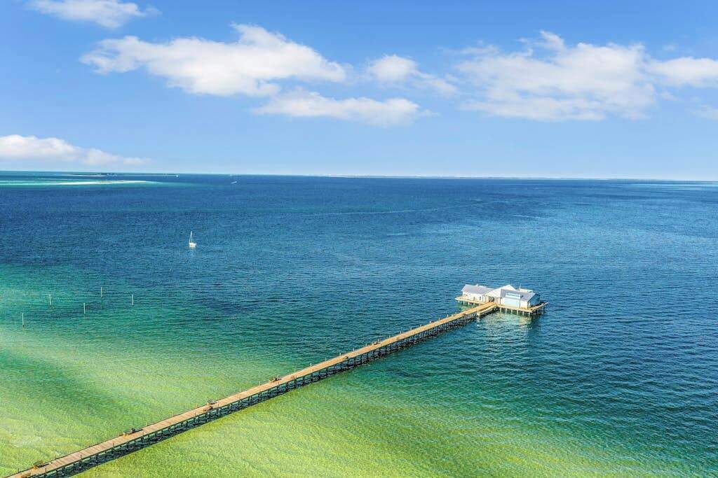 A pier extending into a clear blue sea with a small building at the end.
