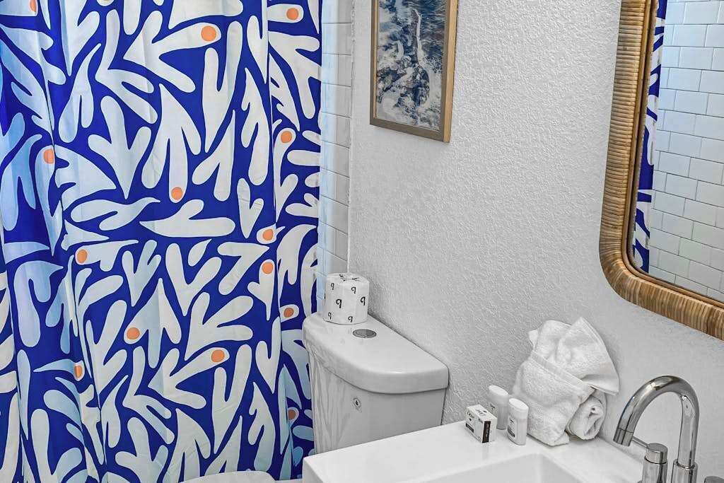 A bathroom with a white sink, a toilet, a shower curtain with a blue and white abstract pattern, and a framed picture on the wall.