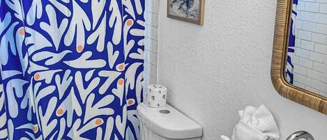 A bathroom with a white sink, a toilet, a shower curtain with a blue and white abstract pattern, and a framed picture on the wall.