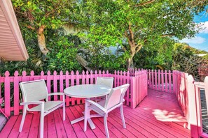 Una terraza rosa con una mesa y sillas, rodeada por una cerca rosa y abundante follaje.