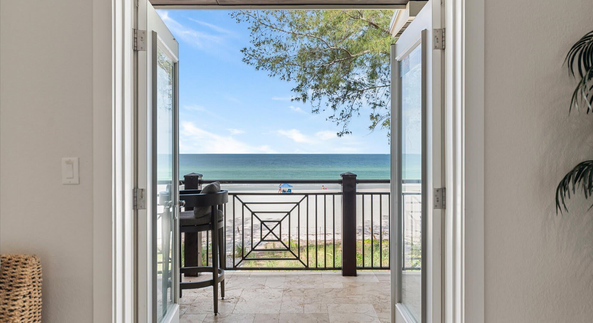 Una porta aperta che dà su un balcone con vista sull'oceano e sulla spiaggia.