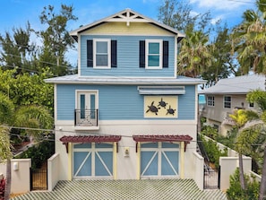 A two-story house with a balcony, garage doors, and a decorative turtle mural. - Luxury oceanfront home w/ pool, spa, free parking (Holmes Beach)
