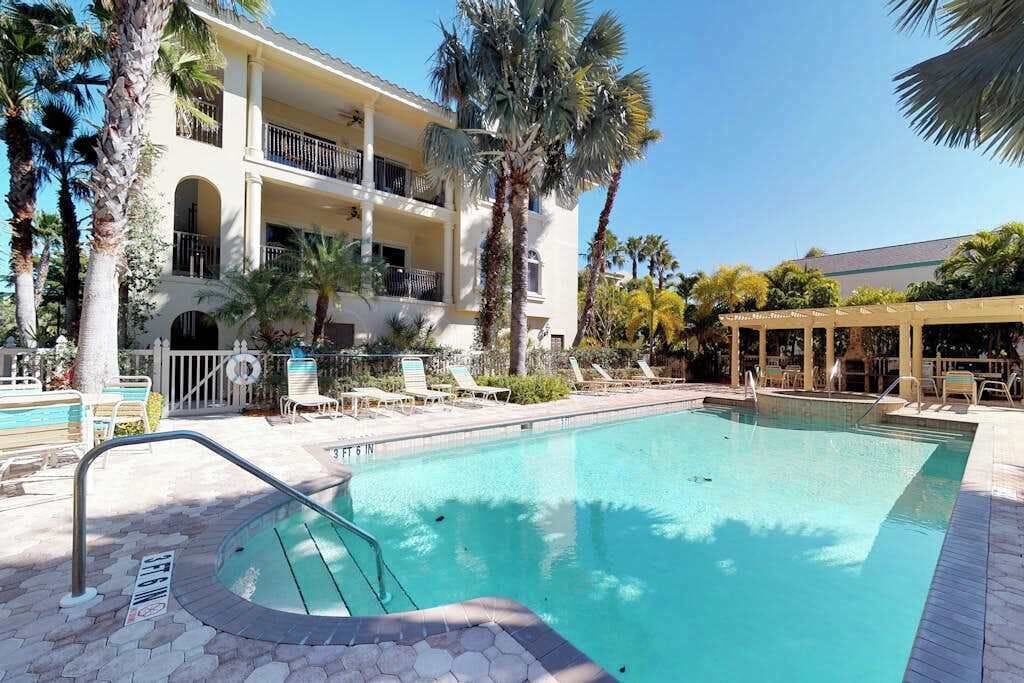 A pool area with a two-story building, palm trees, and lounge chairs.
