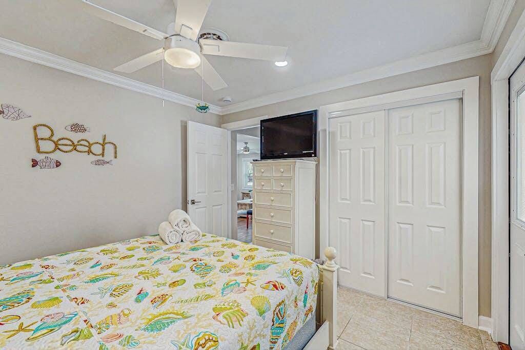 Une chambre à coucher avec un lit, un ventilateur de plafond, une télévision et une armoire.
