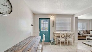 Un coin repas avec une table et des chaises en bois, une porte bleue et une horloge au mur.