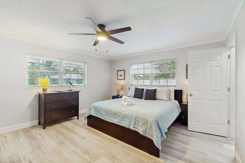 A bedroom with a bed, a dresser, a ceiling fan, and a door.