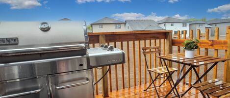 A barbecue grill, wooden deck, and a view of houses in the background.