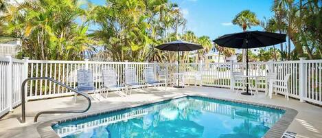 A swimming pool with a white fence, lounge chairs, and umbrellas.