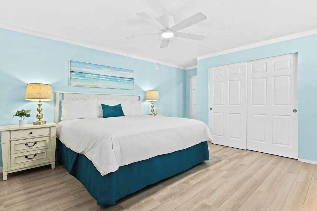 A bedroom with a bed, two bedside tables with lamps, a ceiling fan, and a door.