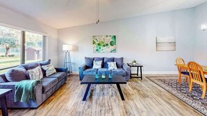 Uma sala de estar com sofá, mesa de centro e cadeiras, área de jantar com mesa e cadeiras, e obras de arte nas paredes.