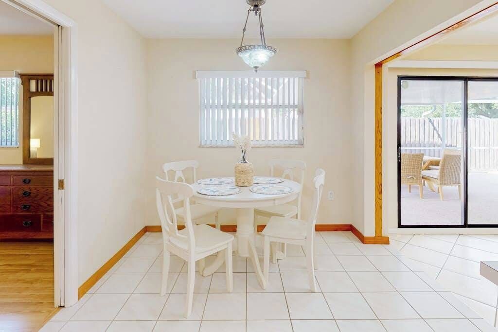 A dining area with a round table, white chairs, a chandelier, and a sliding glass door leading to an outdoor patio.