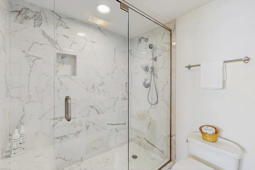 A bathroom with a glass-enclosed shower, a toilet, and a small shelf with toiletries.