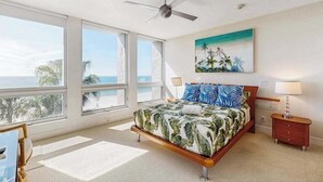 Ein Schlafzimmer mit einem Bett, einem Deckenventilator, einem Nachttisch, einer Lampe und einem Bild mit Strandmotiv.