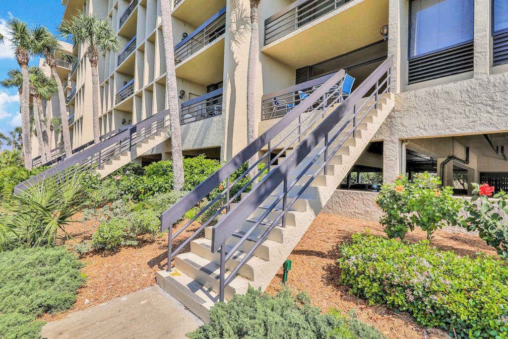A multi-story hotel with outdoor stairs, palm trees, and a landscaped garden.