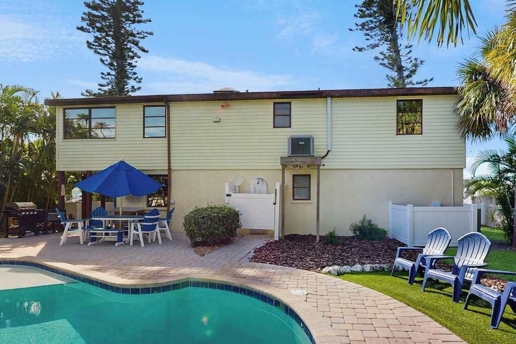 A two-story house with a swimming pool, outdoor seating, and a small garden.