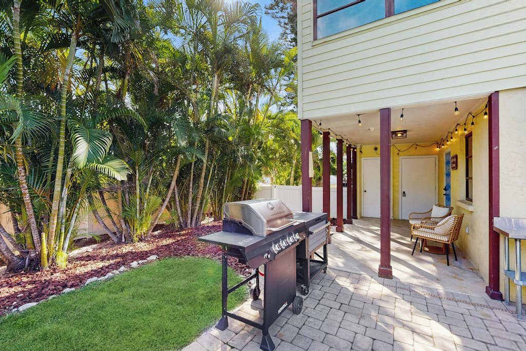Een terras met een barbecue, buitenmeubels en uitzicht op een huis met een overdekte zone.