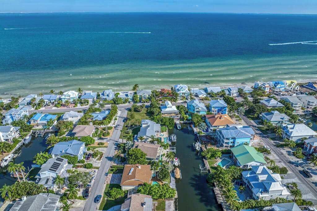 Vista aérea de una zona residencial costera con casas, un puerto deportivo y una vista despejada del océano.