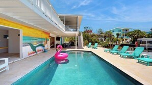 Una piscina con un giuco galleggiante a forma di fenicottero rosa, poltrone da relax color turchese e un murale con il nome 'Anna Maria'.