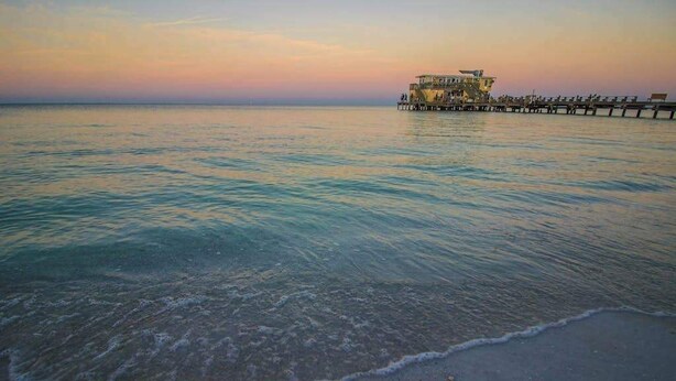 A coastal scene with a pier extending into calm waters, a building on the pier, and a clear sky. - Oceanview getaway with pool & private patio - steps from the beach (Holmes Beach)