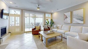 A spacious living room with a fireplace, a ceiling fan, and a large window. - Oceanview getaway with pool & private patio - steps from the beach (Holmes Beach)