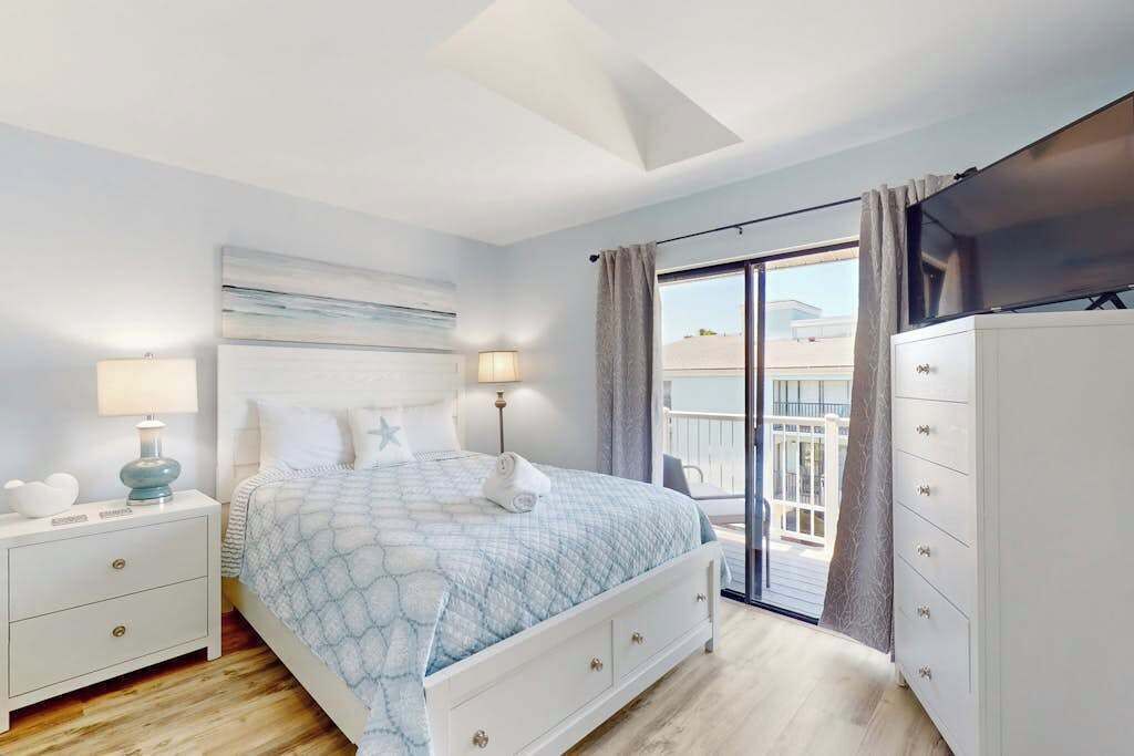 Een slaapkamer met een bed, nachtkastjes, een dressoir en een balkon met uitzicht.