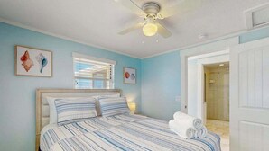 Une chambre à coucher avec un lit, un ventilateur de plafond et des œuvres d’art accrochées au mur.
