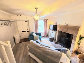 A cozy living room with a sofa, a television, a fireplace, and a window with curtains. - Cosy Cottage with river stream in Matlock (Matlock)