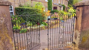 A gated entrance to a residential area with stone buildings, a sign indicating private property, and a variety of plants and flowers. - Cosy Cottage with river stream in Matlock (Matlock)
