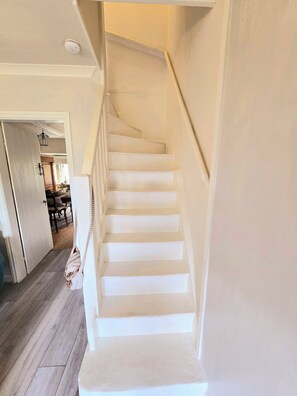 A white staircase leading to an upper floor with a light fixture above. - Cosy Cottage with river stream in Matlock (Matlock)