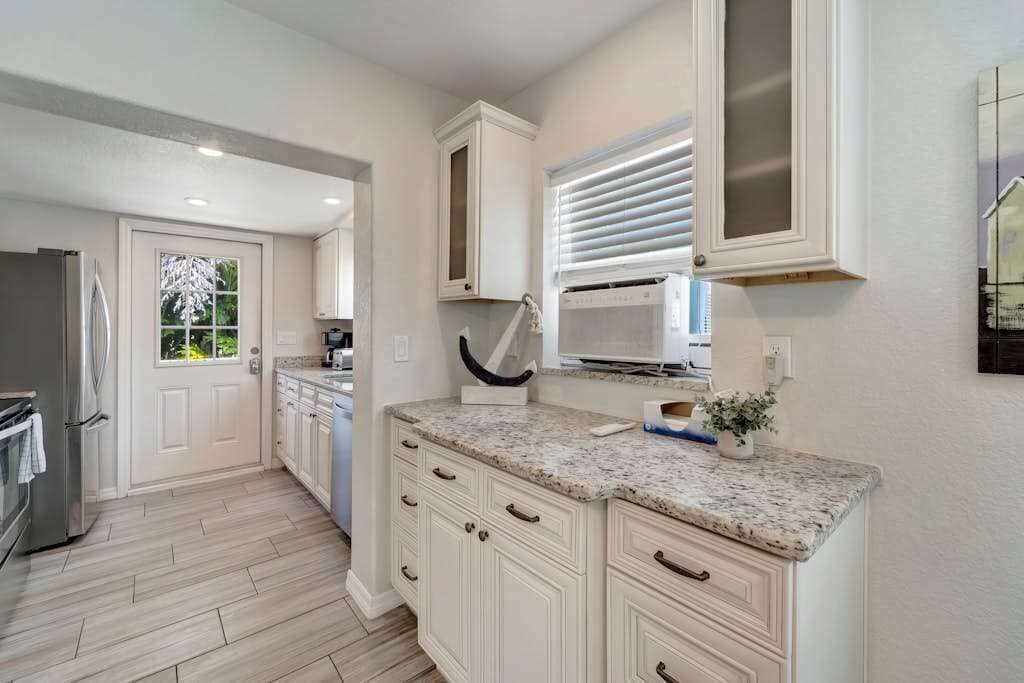 A kitchen with white cabinetry, a granite countertop, a microwave, and a window with blinds.
