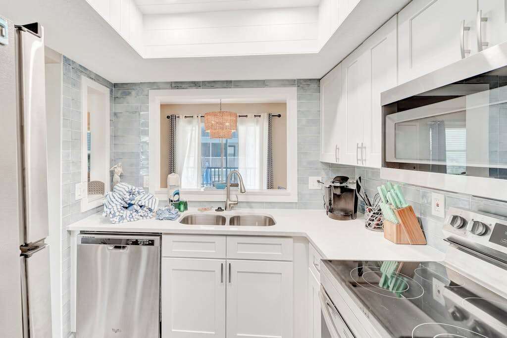 A modern kitchen with white cabinetry, a stainless steel dishwasher, a double sink, a microwave, and an oven.