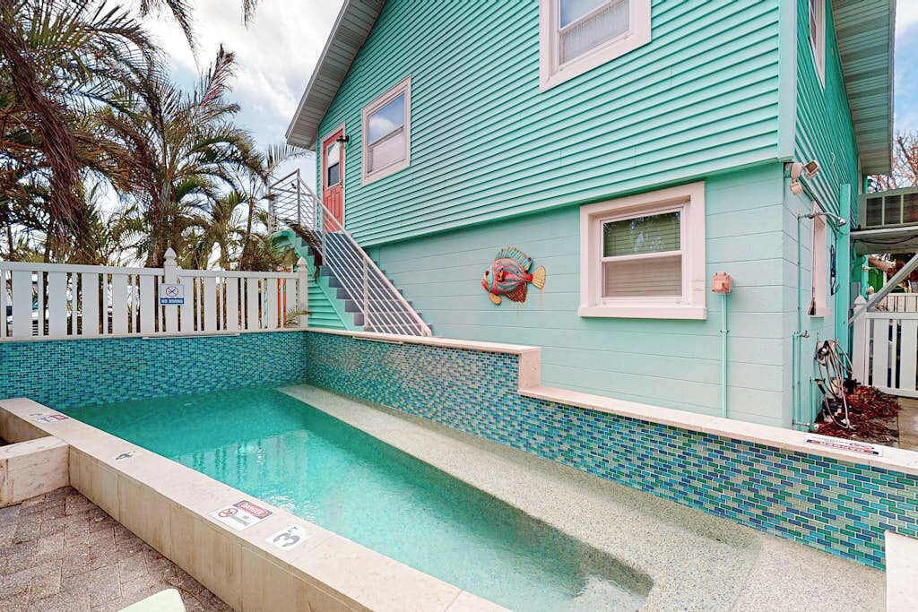 Un edificio turquesa con piscina, una escalera y una valla blanca.