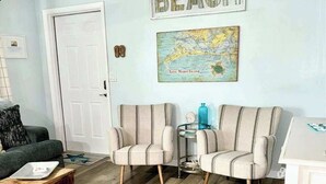 A living room with two striped armchairs, a small round table, a map on the wall, and a door. - 2nd-floor condo with heated pool - walk to beach & Bridge Street (Bradenton Beach)