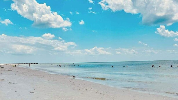 A beach with a pier extending into the water, people swimming and walking along the shore. - 2nd-floor condo with heated pool - walk to beach & Bridge Street (Bradenton Beach)