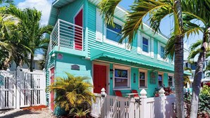 A turquoise two-story house with a red door, white railings, and a small balcony. - 2nd-floor condo with heated pool - walk to beach & Bridge Street (Bradenton Beach)