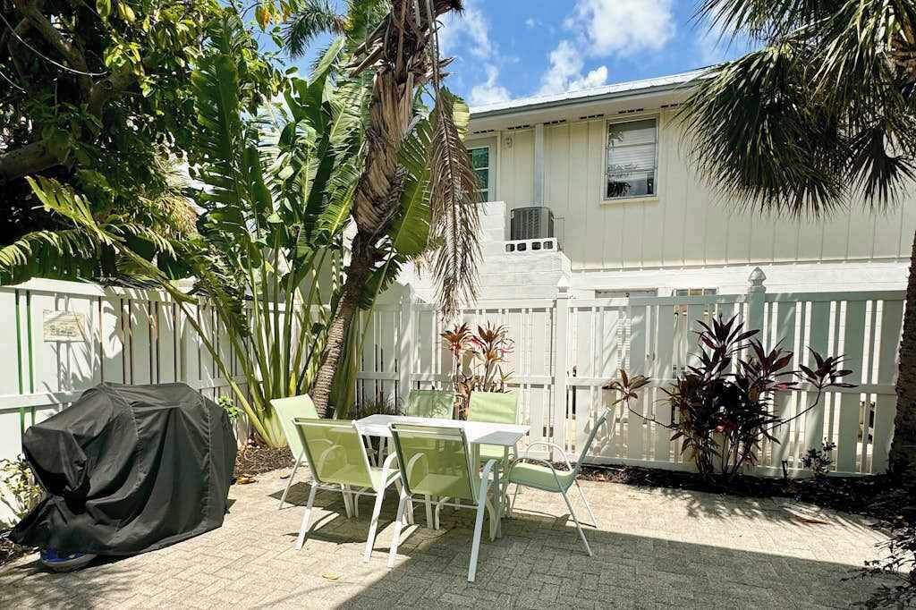 A patio with a table and chairs, a covered object, and a white fence.