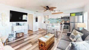A modern living room with a sofa, coffee table, and TV. There's a dining area with a table and chairs. The kitchen has a microwave, oven, and refrigerator. - 2nd-floor condo with heated pool - walk to beach & Bridge Street (Bradenton Beach)