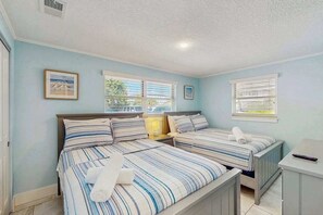 A bedroom with two beds, a window with blinds, a bedside table, and a framed picture on the wall. - Cozy Beachfront Villa | Direct Gulf Access | Free Parking, W/D (Holmes Beach)