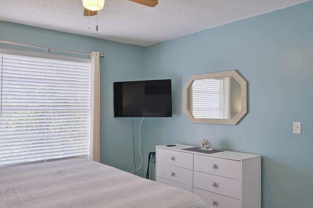 A bedroom with a bed, a dresser, a TV, and a window with blinds.