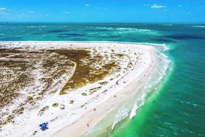 Vista aérea de uma praia com águas turquesa cristalinas, uma faixa de areia e vegetação rala.