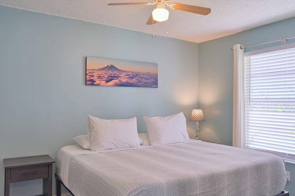 Quarto com cama, mesa de cabeceira, ventilador de teto, luminária na parede e janela com persianas.