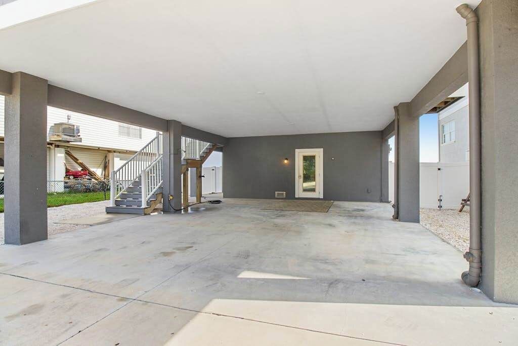 Un patio abierto con piso de concreto, una sección cubierta con techo blanco y una escalera que lleva a un nivel superior.