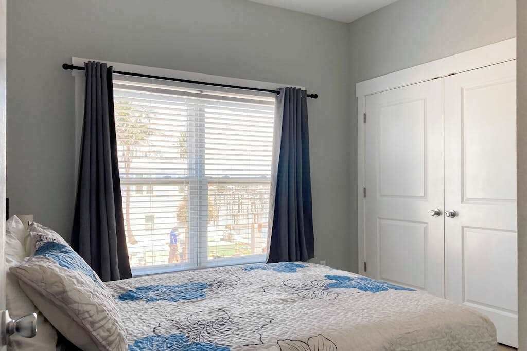 A bedroom with a bed, a window with curtains, and a white door.